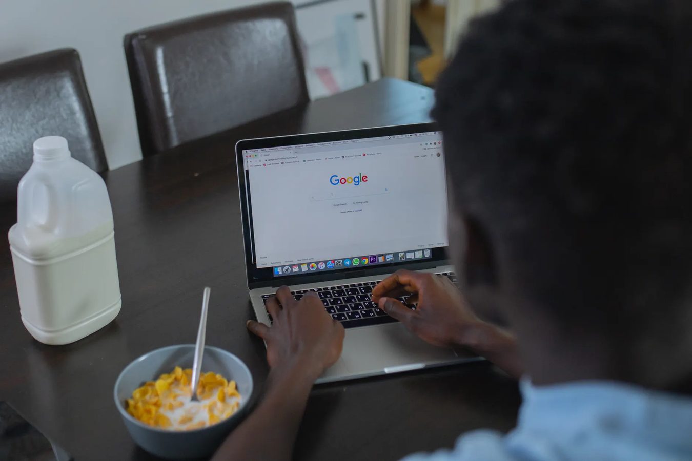 A person working on a laptop at a kitchen table with a notebook beside it